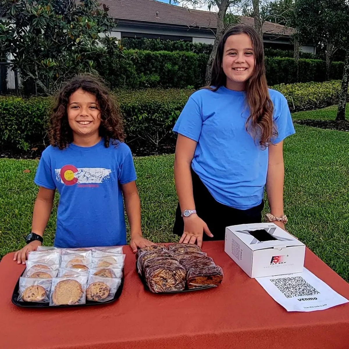 Isabel and Jack smiling behind a table filled with Cookie Corner baked goods